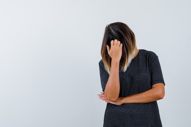 Dame buigt hoofd naar beneden in zwart t-shirt en kijkt depressief, vooraanzicht.