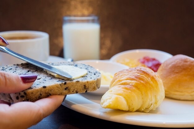 Dame die boter op broodontbijt zet dat met melk en koffie wordt geplaatst