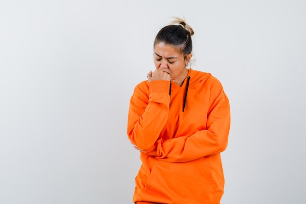 Dame die emotioneel op haar vuist bijt in oranje hoodie en er depressief uitziet