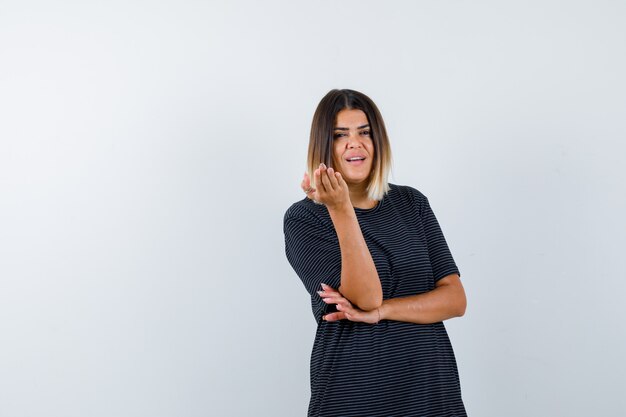 Dame die hand in vragend gebaar in zwart t-shirt opheft en verbaasd kijkt. vooraanzicht.