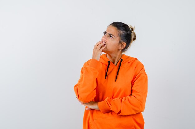 Dame die hand op kin houdt in oranje hoodie en er attent uitziet