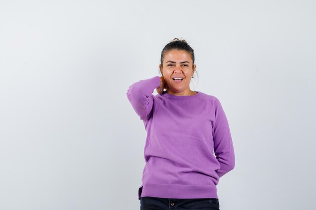 Dame die hand op nek houdt in wollen blouse en er vrolijk uitziet