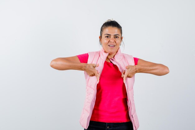 Dame die naar beneden wijst in t-shirt, vest en er zelfverzekerd uitziet