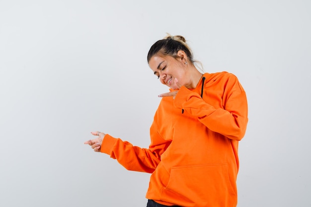 Gratis foto dame die opzij wijst in oranje hoodie en er vrolijk uitziet