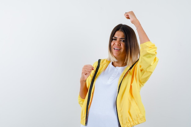 Dame die winnaargebaar in t-shirt, jasje toont en gelukkig, vooraanzicht kijkt.