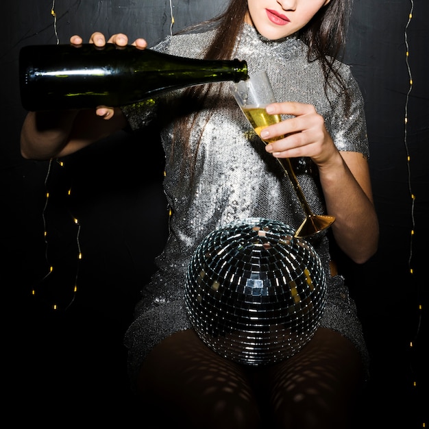 Dame gietende champagne in glas dichtbij discobal