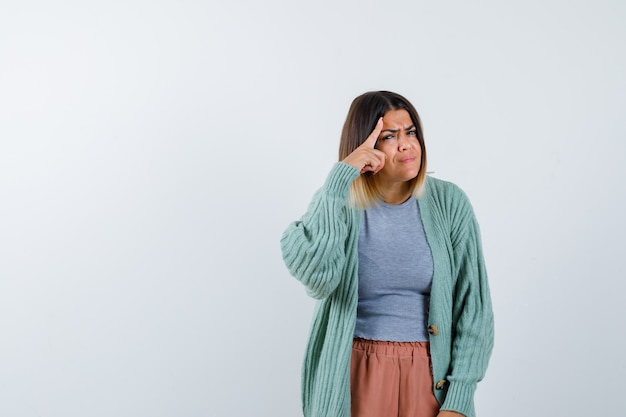 Dame houdt vinger op hoofd in vrijetijdskleding en kijkt serieus, vooraanzicht.