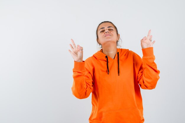 Dame in oranje hoodie die meditatiegebaar toont en er vredig uitziet