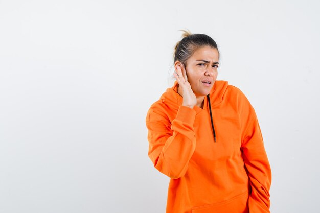 Dame in oranje hoodie die privégesprek afluistert en er verward uitziet