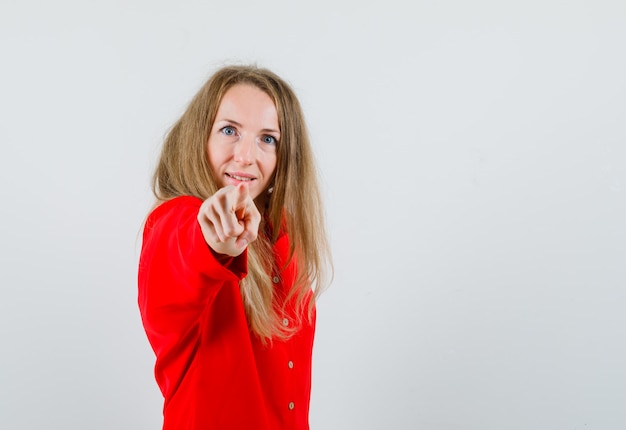 Dame wijzend op camera in rood shirt en kijkt zelfverzekerd,