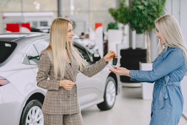 Dames in een autosalon. Vrouw die de auto koopt. Elegante vrouw in een blauwe jurk. Manager geeft sleutels aan de klant.