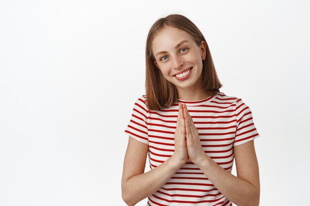 Dank u. Aangename glimlachende blonde vrouw toont namaste, waarderingsgebaar, groet, bedankt, uiting van dankbaarheid, ziet er gelukkig en gevleid uit, witte achtergrond.