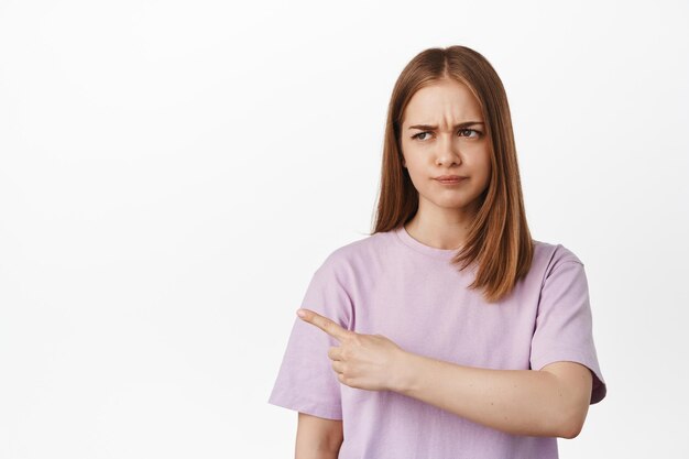 Dat het slecht is. Ontevreden blonde vrouw die wijst, wenkbrauwen fronst met afkeer, starend naar iets met een oordelend gezicht, met een vreselijk bannerlogo aan de linkerkant, klagend, witte achtergrond