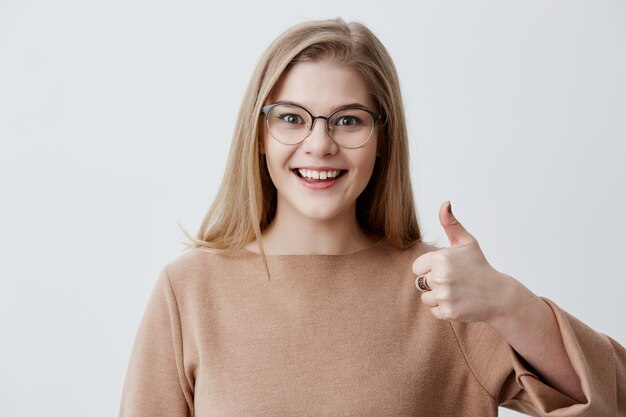 Dat vind ik leuk. Goed werk. Gelukkig jong blondevrouw die toevallige lange mouwen dragen die duimen maken omhoog teken ondertekenen en vrolijk glimlachen, tonend haar steun en respect aan iemand. Lichaamstaal