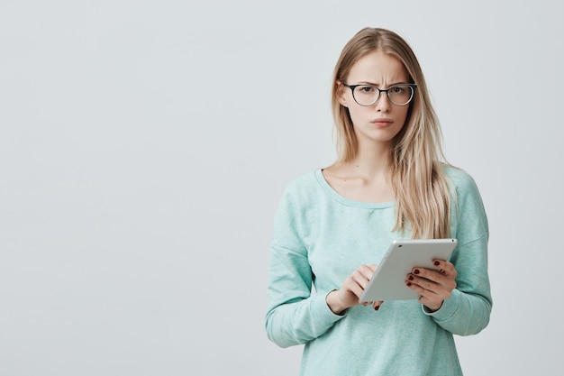 De aantrekkelijke blondebeambte in eyewear werkt met digitale tablet