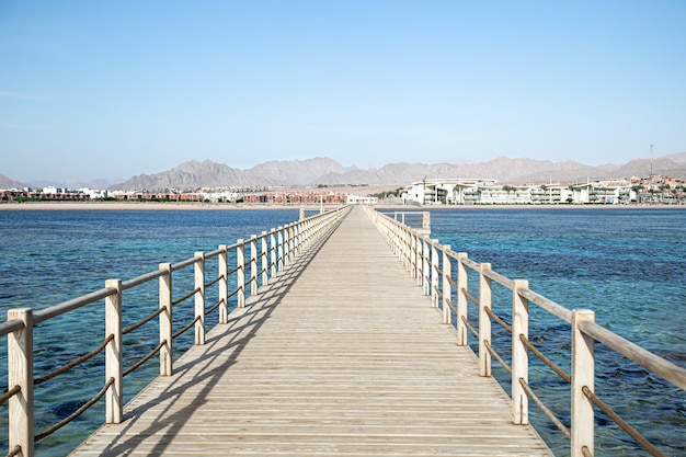 De achtergrond is een mooie lange houten pier tussen de oceaan en de bergen.