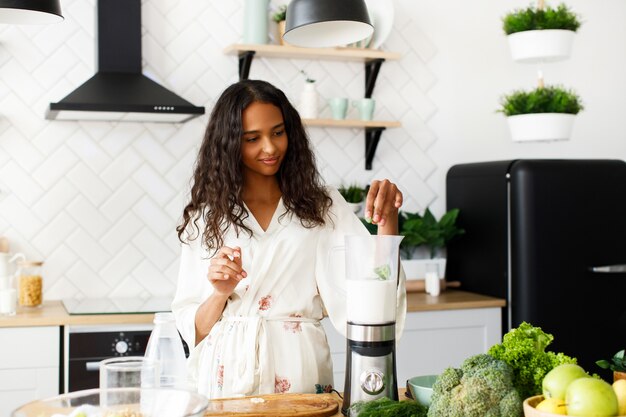 De Afrikaanse vrouw maakt milkshake in een mixer in de ochtend