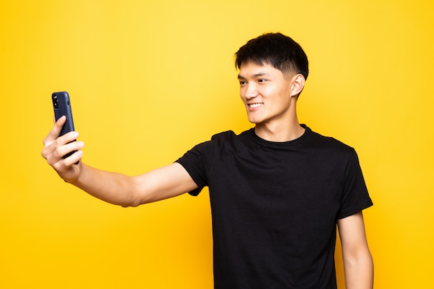 De Aziatische Chinese telefoon van de mensenholding over geïsoleerde gele muur