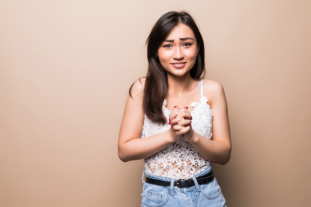 De Aziatische jonge vrouw over geïsoleerde beige muur houdt palm samen. Persoon vraagt iets