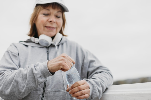 De bejaarde vrouw van Smiley met waterfles en hoofdtelefoons in openlucht