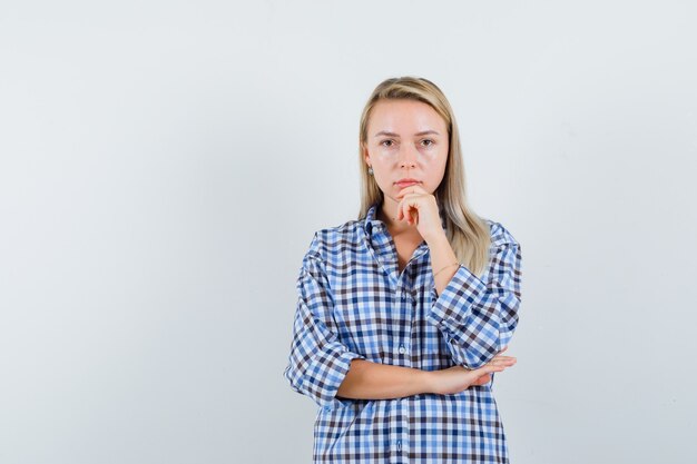 De blonde dame die zich in het denken bevindt stelt in geruit overhemd en ziet er verstandig uit