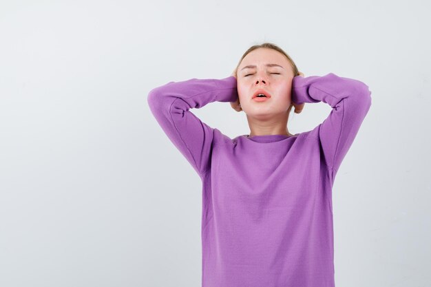 De blonde vrouw bedekt haar oren met handen op een witte achtergrond