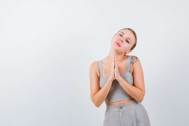 De blonde vrouw bedelt door handen vast te houden op de borst op een witte achtergrond