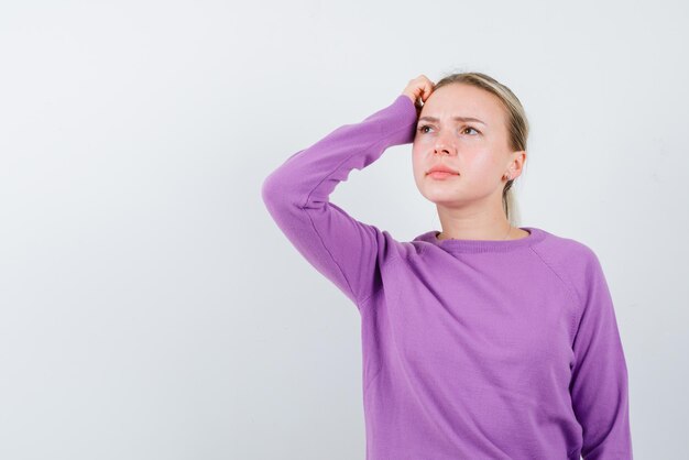 De blonde vrouw denkt door haar hand op het hoofd op een witte achtergrond te leggen