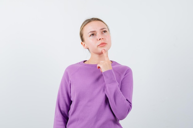 De blonde vrouw denkt door haar wijsvinger op de kin op een witte achtergrond te houden