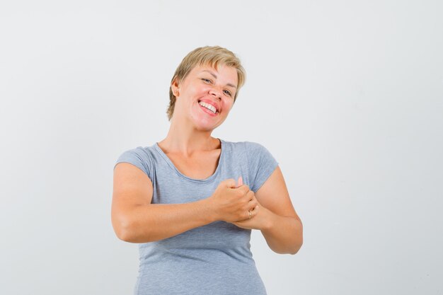 De blonde vrouw die haar handen wrijft in lichtblauw t-shirt en gelukkig, vooraanzicht kijkt.