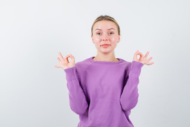 De blonde vrouw vertoont een goed gebaar met handen op een witte achtergrond