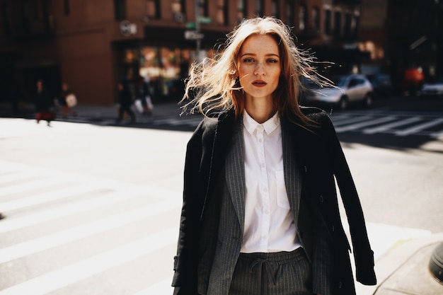 De blondedame in zwarte laag bevindt zich op de zonnige straat ergens in de stad van new york