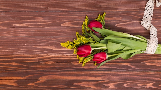 De bos van rode tulpenbloemen en goldenrod bloemen klopten met kant tegen houten achtergrond