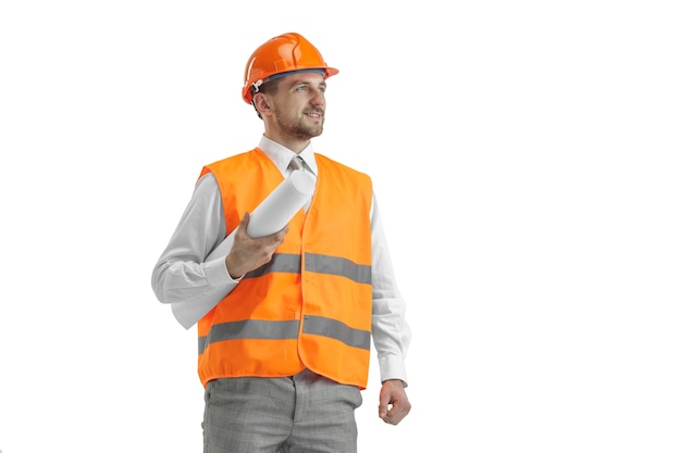De bouwer in een bouwvest en een oranje helm die zich op witte muur bevindt. Veiligheidsspecialist, ingenieur, industrie, architectuur, manager, beroep, zakenman, baanconcept