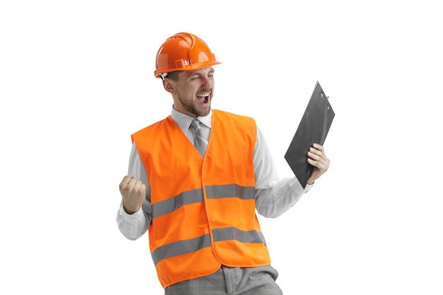 Gratis foto de bouwer in een bouwvest en een oranje helm die zich op witte muur bevindt. veiligheidsspecialist, ingenieur, industrie, architectuur, manager, beroep, zakenman, baanconcept