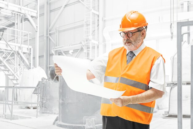 De bouwer in een bouwvest en een oranje helm die zich op witte studiomuur bevindt