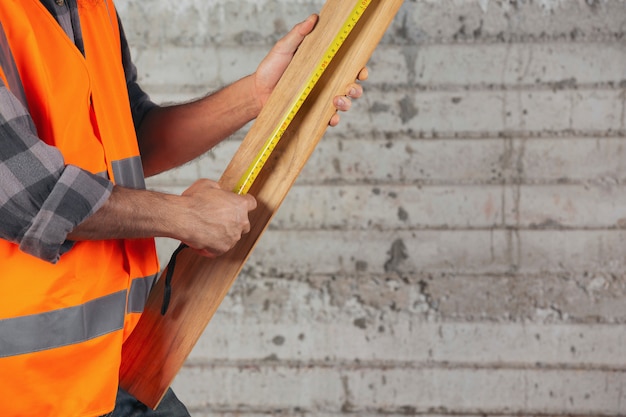 De bouwvakker draagt houten planken met Meetlint op bouwwerf.