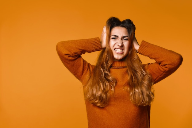 De boze roodharige kaukasische vrouw kleedde zich in trui met handen op haar hoofd