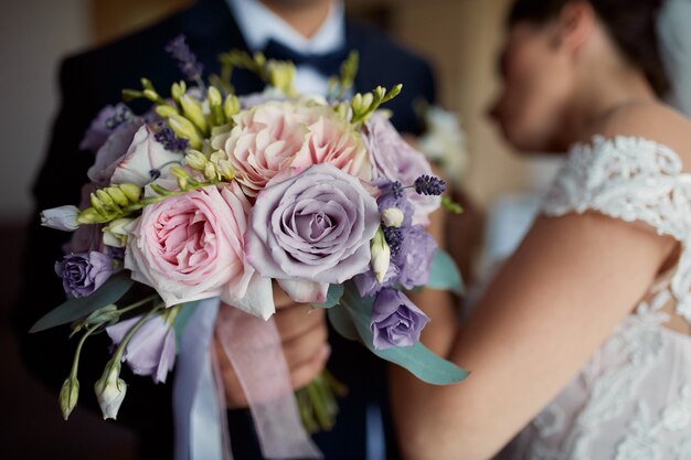 De bruid speldt boutonniere aan het jasje van de bruidegom terwijl hij huwelijksboeket houdt