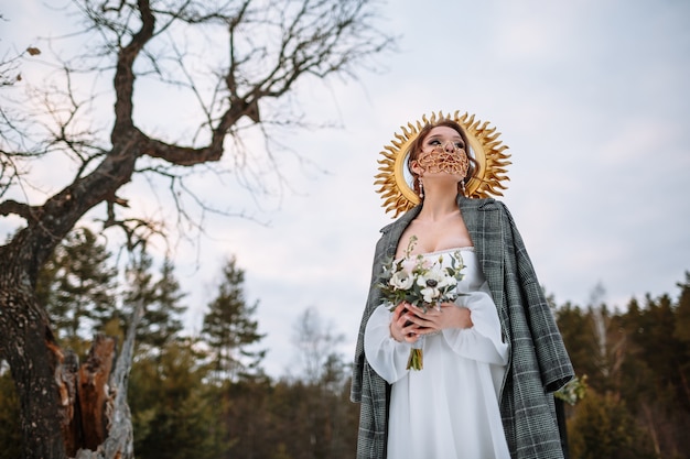 De bruid staat in een besneeuwd bos. de bruid met een fantastisch beschermend masker.