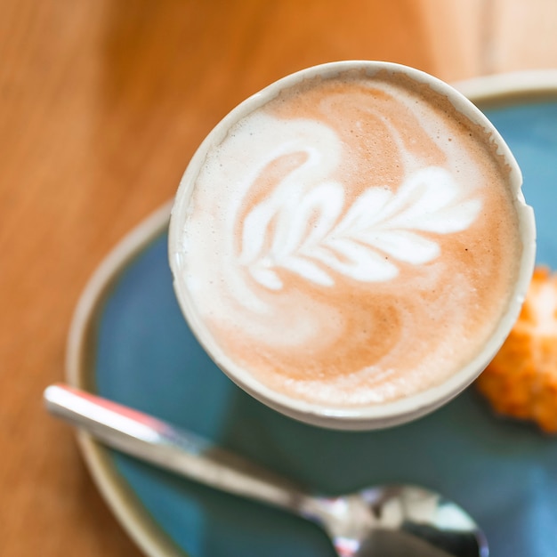 De cappuccinoschuim van de koffie latte kunst in kop op houten lijst