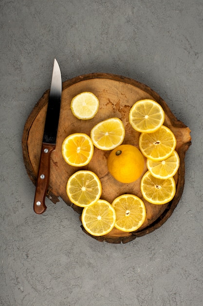 Gratis foto de citrusvruchten sneden een citroenplakken van bovenaanzicht op het bruine houten bureau en op de grijze vloer