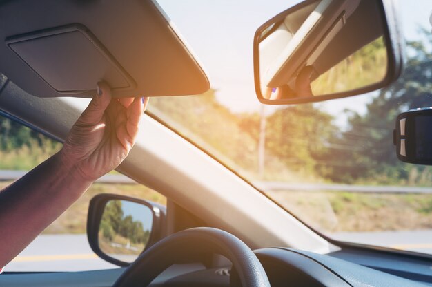 De dame past zonnescherm aan terwijl het drijven van auto op wegweg - binnenlandse auto die concept gebruiken