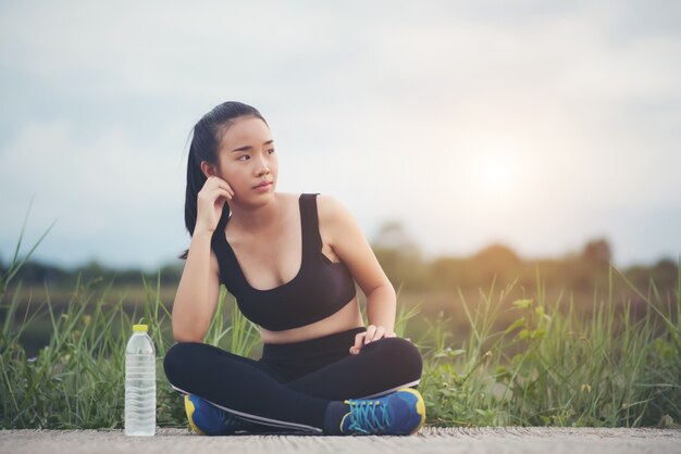 De de vrouwenagent van de fitness gaat zitten ontspannend met waterfles na buiten opleiding in park