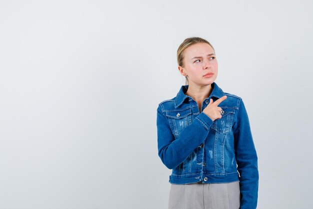 De denkende blonde vrouw wijst naar rechts met wijsvinger op witte achtergrond