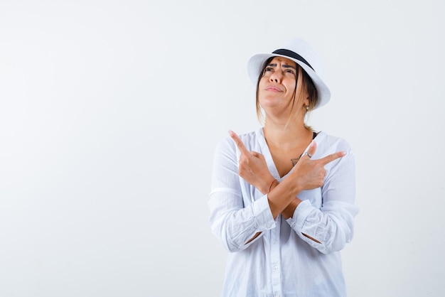 Gratis foto de denkende vrouw wijst zijwaarts met gekruiste handen op een witte achtergrond