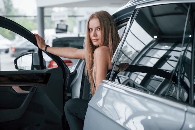 De deur openen. Meisje en moderne auto in de salon. Overdag binnenshuis. Een nieuw voertuig kopen