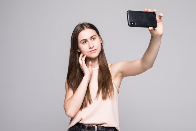 De donkerbruine vrouw neemt selfie met slimme telefoon die op wit wordt geïsoleerd