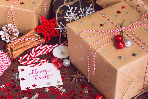 De doos van de de vakantiegift van kerstmis met prentbriefkaar vrolijke kerstmis op verfraaide feestelijke lijst met denneappelskaneel