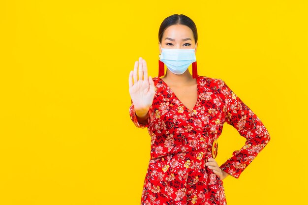 De draagmasker van de portret mooi jonge aziatische vrouw voor beschermt coronavirus of covid19 op gele muur